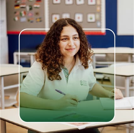 A smiling Nadeen School student at her desk in a classroom