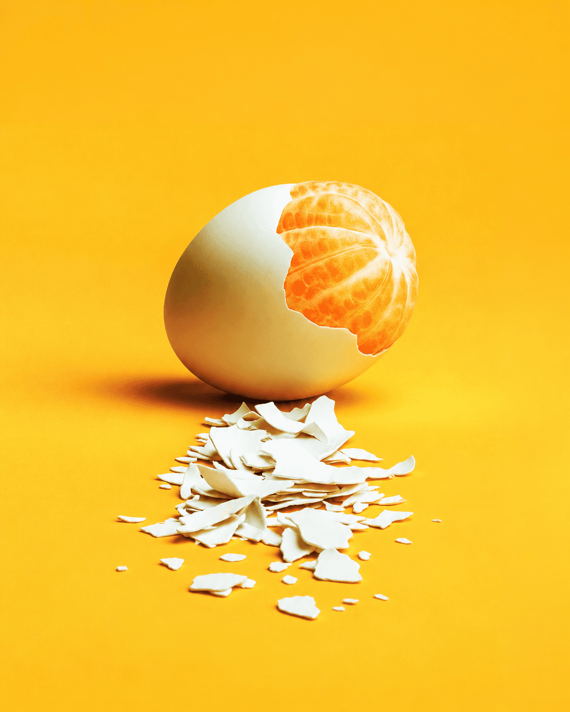 A peeled orange inside a cracked eggshell, with shell pieces scattered in front