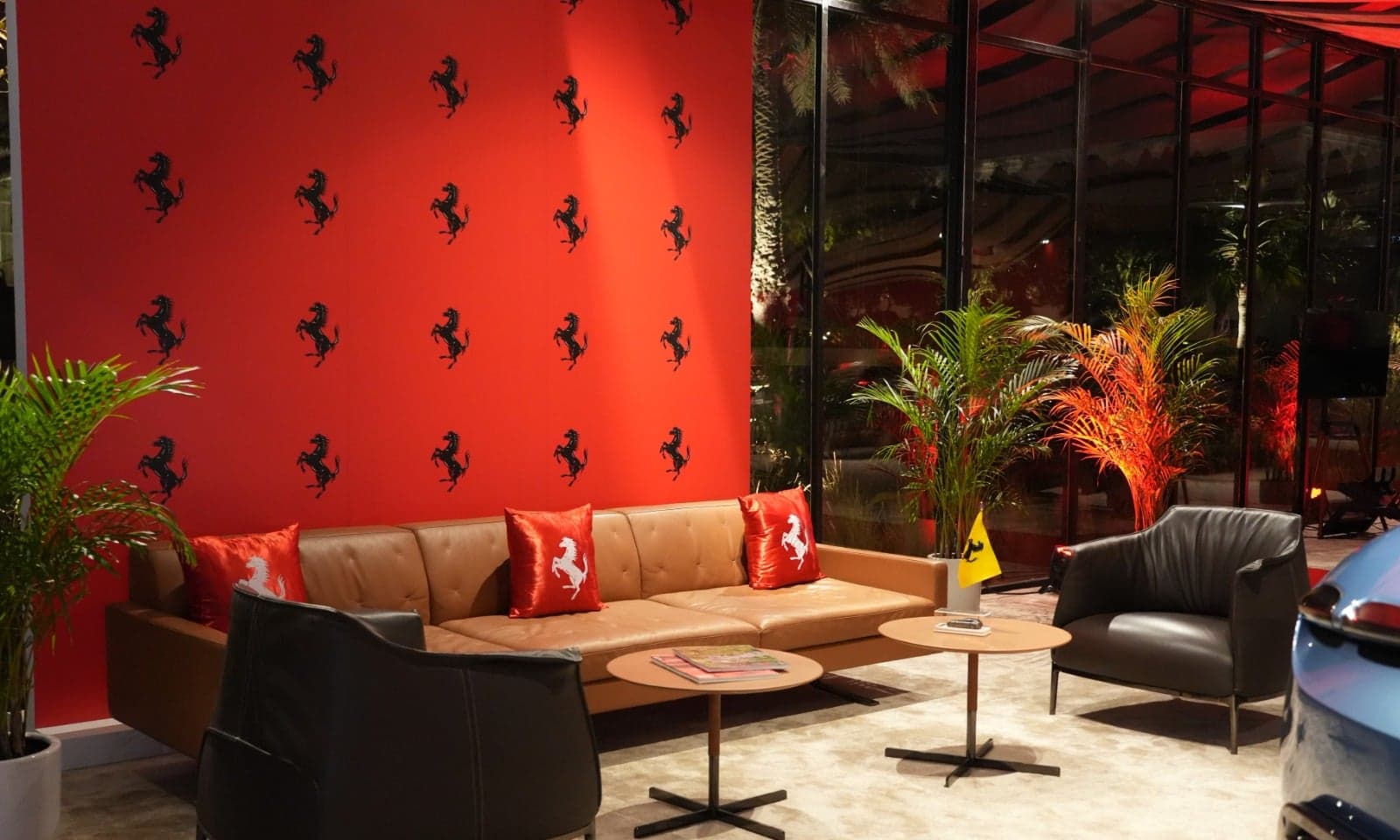 A Ferrari Pavilion lounge: a tan leather sofa with prancing-horse cushions against a red wall of black Ferrari horses